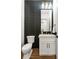 Stylish powder room featuring black accent wall, wood floors, white vanity and gold fixtures at 1626 Burtonwood Cir, Charlotte, NC 28212