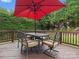 A wooden deck with a black table, umbrella, four chairs, and a green backdrop of trees and bushes at 8921 Whittingham Dr, Waxhaw, NC 28173