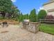 Stone outdoor kitchen and grilling area on a stone patio with green landscaping and manicured green hedges at 8921 Whittingham Dr, Waxhaw, NC 28173