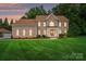 Brick two-story home featuring a manicured lawn and covered front porch with sunset in the background at 6324 Old Fox Hunt Ln, Mint Hill, NC 28227