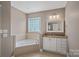 Bright main bathroom featuring a soaking tub, granite vanity, and a glass block window at 15830 Waterfront Dr, Huntersville, NC 28078
