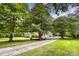 Brick home with a long driveway and attached carport nestled among mature trees and greenery at 1010 Forest Dr, Lancaster, SC 29720