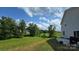 Wide backyard with beautiful green lawn, tree line, blue skies, and a gas grill off the concrete patio at 347 Carolina Hemlock Dr, Locust, NC 28097