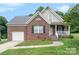 Charming brick home features a covered front porch, attached garage, and well-maintained lawn under a blue sky at 5111 Clearwater Rd, Charlotte, NC 28217
