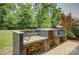 Outdoor cooking area with stone grill, wood storage, and a built-in smoker on a paved patio surrounded by trees at 15344 Cimarron Hills Ln, Charlotte, NC 28278