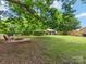 Expansive backyard with lush green grass, a fire pit, storage shed, garden area, and mature trees at 3042 Cresthill Dr, Charlotte, NC 28212