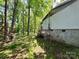 View of the side of the home with mature trees, natural landscaping, and a partially visible basement foundation at 1399 Branton Dr, Iron Station, NC 28080