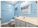 Quaint bathroom with a single sink vanity, a toilet, light blue walls, and a mirror with a window for natural light at 105 Saddlewood Ln, Statesville, NC 28625