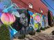 Outdoor mural painted on a brick wall featuring various images and colors near a sidewalk at 1315 Charles Ave, Charlotte, NC 28205