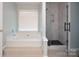Bright bathroom showcasing a tub and glass enclosed shower with marble-like tile at 5741 Bentgrass Run Dr, Charlotte, NC 28269