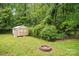 Private backyard featuring a storage shed, fire pit, mature trees, and lush green grass at 7725 Whitmire Ln, Mint Hill, NC 28227
