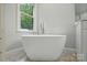 A modern white free standing tub with sleek fixtures sits beneath a window at 7725 Whitmire Ln, Mint Hill, NC 28227