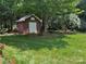 A backyard featuring a small storage shed, surrounded by green grass and flowering trees at 102 Rosewood Ln, Locust, NC 28097
