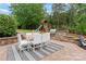 Outdoor dining area featuring a stone grill, play set and table with white chairs and lush landscaping at 13716 Glen Abbey Dr, Charlotte, NC 28278