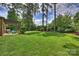 Lush backyard features a covered patio with outdoor seating surrounded by mature trees and green grass at 3032 Kings Manor Dr, Matthews, NC 28104