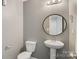 A half bath features a sleek pedestal sink, toilet, and a round mirror at 5311 Oakdale Ridge Rd, Charlotte, NC 28216