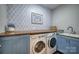 Convenient laundry room featuring side-by-side washer and dryer and utility sink with blue and white patterned wallpaper at 2593 Las Brisas Ln, Denver, NC 28037