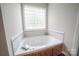 Bathroom showcases a luxurious soaking tub with marble tile surround and natural light from a glass block window at 8259 Camelia Ln, Denver, NC 28037