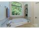 Bright bathroom featuring a soaking tub, large window overlooking trees, and decorative shelving niche at 2314 Winding Oaks Trl, Waxhaw, NC 28173