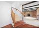 Interior staircase with wooden handrail leading to a living room featuring a stone fireplace and wood beam ceilings at 24008 Carriker Rd, Albemarle, NC 28001