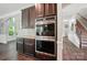 Gourmet kitchen with stainless steel double oven, dark cabinets, and granite countertops next to staircase at 16229 Loch Raven Rd, Huntersville, NC 28078
