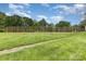 Fenced tennis court surrounded by lush green lawns and mature trees under a bright blue sky with fluffy white clouds at 6203 Rosecroft Dr, Charlotte, NC 28215