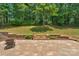 Open backyard view from a paved patio with stone retaining walls, lush greenery, and a distant wooded area at 9423 Wood Ridge Dr, Charlotte, NC 28277