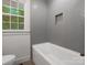 Bathroom with white bathtub and gray brick-like tiling on the walls by the window at 4126 Howie Cir, Charlotte, NC 28205
