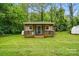 Charming exterior of a small, tan cottage featuring a wooden deck and lush green lawn at 1621 California Rd, York, SC 29745