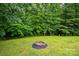 Well-manicured backyard with a stone fire pit and lush green grass, framed by mature trees and shrubbery at 4059 Caitlins Way, Hickory, NC 28602