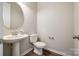 A neutral powder room with wood-look floors, toilet and a pedestal sink with a round mirror at 173 Morgans Branch Rd, Belmont, NC 28012
