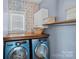Functional laundry room with front-loading washer/dryer, wood countertop, floating shelf, wall cabinet, and decorative wallpaper at 1849 Still Water Ln, Indian Land, SC 29707