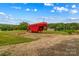View of red horse trailer on grassy field surrounded by trees under a blue sky with clouds at 296 Hicks Creek Rd, Troutman, NC 28166