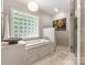 Bright bathroom with marble tile, tub, glass block window, and walk-in shower at 4026 Sharon View Rd, Charlotte, NC 28226