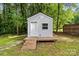 This shed features gray siding, a sturdy front deck, and a window, nestled in a wooded lot at 704 W Border St, Dallas, NC 28034