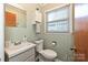 Cozy bathroom with a toilet, sink, mirror, window with blinds, and storage cabinet at 267 Buffalo Nw Ave, Concord, NC 28025