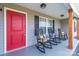 Inviting front porch with rocking chairs and a bright red door, framed by classic wooden columns and decorative lighting at 2737 Bobcat Rd, Heath Springs, SC 29058