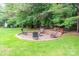 Backyard features a brick firepit with chairs, surrounded by a well-manicured lawn and mature trees at 19625 Callaway Hills Ln, Davidson, NC 28036