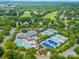 An aerial view displays a neighborhood with golf course, tennis courts, and a luxurious pool, all surrounded by verdant trees at 9210 Ginhouse Ln, Charlotte, NC 28277