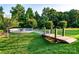 Lush green backyard featuring a stone fire pit area accessed by a charming wooden bridge on a sunny day at 159 Holly Ridge Dr, Mooresville, NC 28115