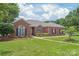A view of a classic brick home with lush green lawn, blooming bushes, and manicured landscaping under a bright sky at 502 Roxanne Nw Ct, Concord, NC 28027