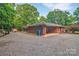 Brick house with a covered parking area and a gravel driveway surrounded by lush trees at 514 Wood St, Troy, NC 27371