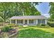 Charming white brick home featuring black shutters, a lush front lawn, and mature trees at 6938 Wrentree Dr, Charlotte, NC 28210