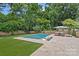 Beautiful backyard pool area with travertine tile, artificial turf, and stylish outdoor seating and umbrella at 6946 Woodstock Dr, Charlotte, NC 28210