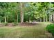 Green backyard with trees and shrubs leading to a stone fire pit area, creating a serene outdoor retreat at 10927 Thornhill Club Dr, Charlotte, NC 28277