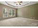 Bright main bedroom with plush carpet, tray ceilings, a ceiling fan, and three large windows at 56119 Finches Ct, Indian Land, SC 29707