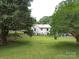 Expansive backyard with mature trees surrounding a white brick home, perfect for outdoor activities at 1614 Linwood Rd, Gaston, NC 28052