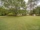Extensive green backyard featuring a mature shade tree and partial view of the white brick home at 1614 Linwood Rd, Gaston, NC 28052