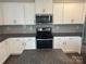 Well-lit kitchen features white cabinets, stainless steel appliances, and a gray backsplash at 9730 Tea Garden Dr, Gastonia, NC 28056