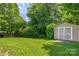 Spacious backyard featuring green grass, a storage shed, and lush trees at 1209 Danielle Downs Se Ct, Concord, NC 28025